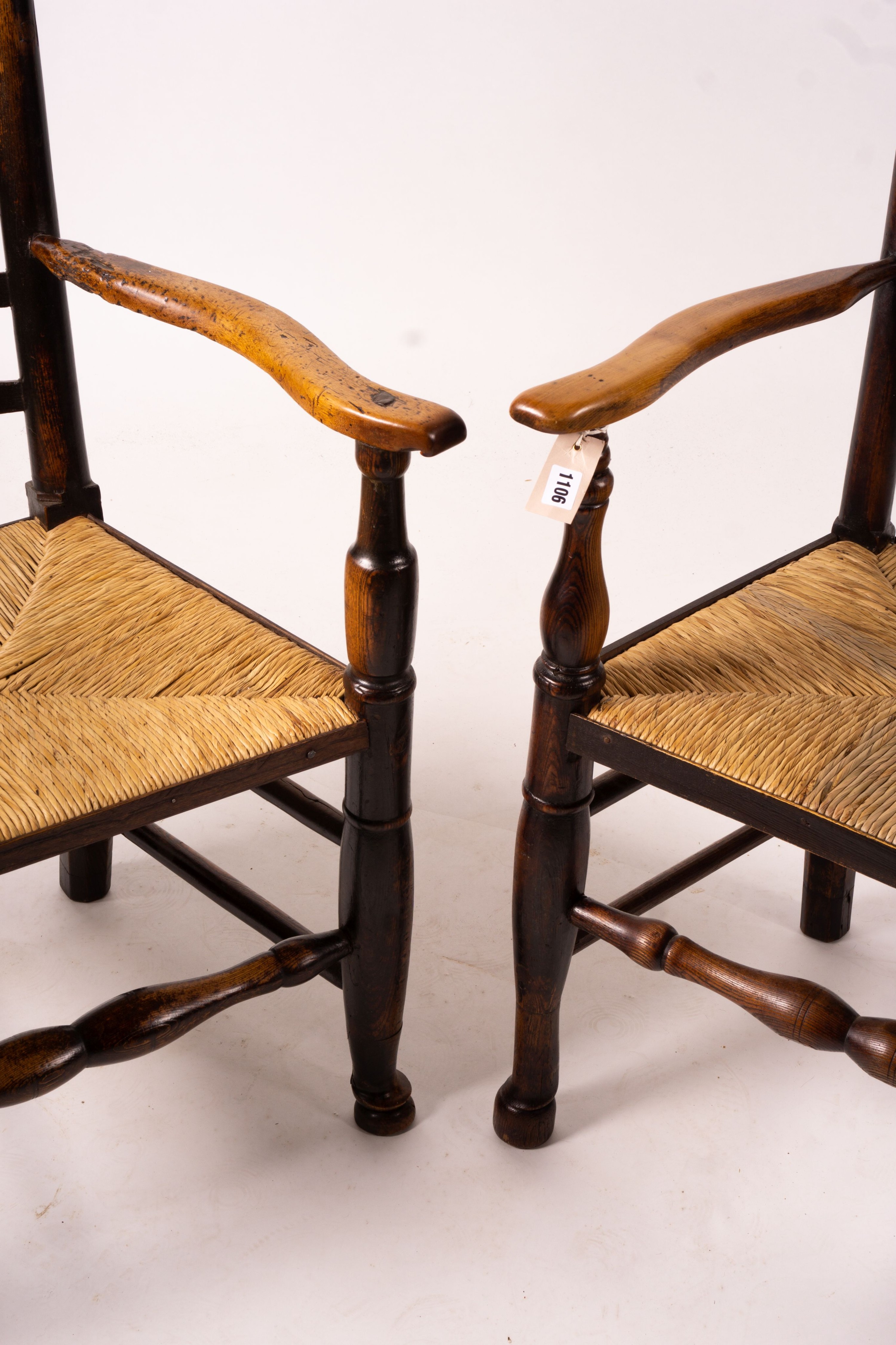 A pair of early 19th century Lancashire ash and fruitwood rush seat ladderback elbow chairs, width 60cm, depth 46cm, height 110cm